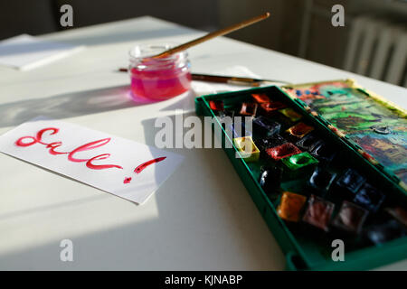Watercolor inscription Sale on white sheet of paper, on table in Stock Photo