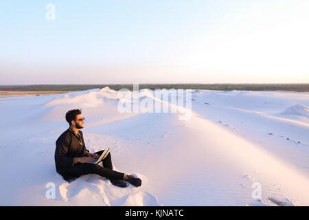 Handsome young Arab man writes on Internet using laptop and sits Stock Photo