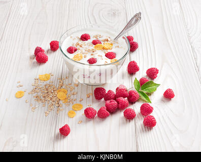 Bowl of homemade yogurt with muesli and fresh raspberry on wooden table. Fresh yogurt. Healthy food concept. High resolution product. Stock Photo