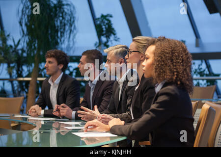 A group of business people sit at a table in a line and are discussing. Stock Photo