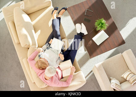 High angle view of a relaxed senior couple reading a book together on the sofa at home. Stock Photo