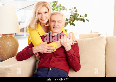 Shot of a loving wife embracing her husband from behind while at home in living room. Stock Photo