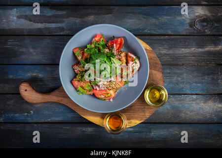 Salad from tomatoes onion parsley and two kinds of oil with sesame seeds on a wooden board. Top view Stock Photo