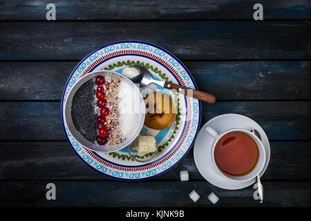 Sweet rice porridge with berries nuts and coconut chips, top view. Healthy breakfast or dessert. Tea and bread with butter. Stock Photo