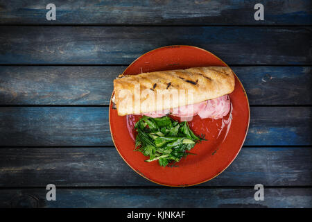 Delicious sandwich with ham mushrooms and green salad on a ceramic plate. Colored wooden background. Top view Stock Photo