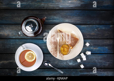 Slice of Cheesecake with jam rafinated sugar and tea kettle with lemon on a colored wooden background. Top view Stock Photo