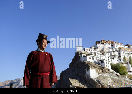 A ladakhi man wearing traditional clothes on the roof of his house, Thikse monastery in the back, Leh, Ladakh, Jammu and Kashmir, India. Stock Photo