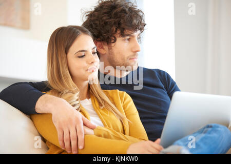 Shot of a young woman using laptop while handsome man sitting next to her and looking thoughtfully. Stock Photo
