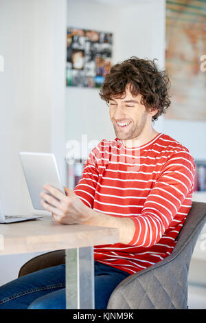 Shot of a casual young man using digital tablet while relaxing at home. Stock Photo