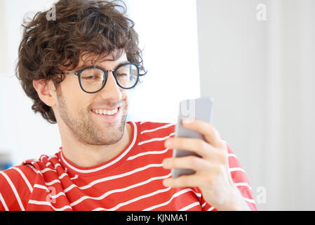 Close-up of a handsome young man using her mobile phone and reading messages while relaxing on sofa at home. Stock Photo