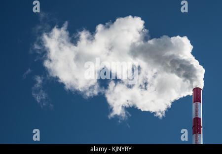 Industrial smokestack in wind. Dirty smoke from red and white factory chimney on blue sky. Stock Photo