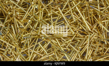 Texture from small decorative nails in golden color. Gleaming gilt pins for jewelry production as background. Stock Photo