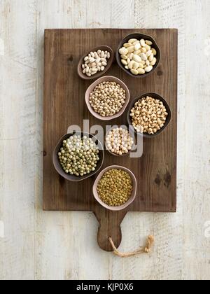 Pulses in bowls on a chopping board, overhead view. Stock Photo