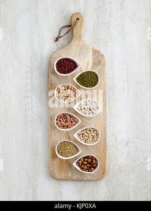 Pulses in tear shaped mini bowls on a chopping board, overhead view. Stock Photo