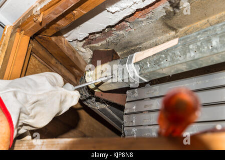 Rolling shutter repairer. Worker, with gloves and screwdriver, adjusts a broken roller shutter of a home Stock Photo