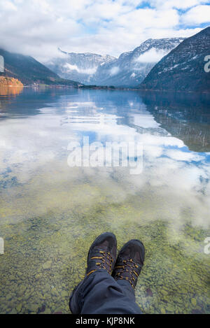 Hiking theme image with a man legs and the Dachstein mountains and their reflection in the Hallstatter lake, in Austria Stock Photo