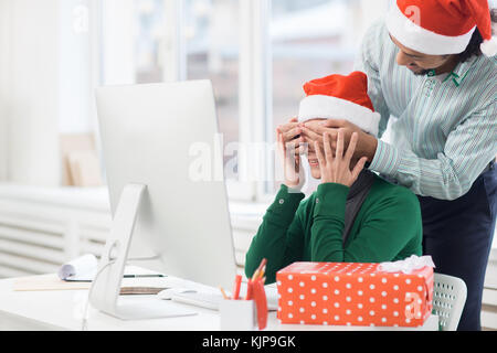 Businesswoman trying to guess who covering her eyes by hands to make her xmas surprise Stock Photo