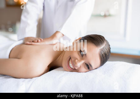 Cheerful young client of spa salon looking at camera while enjoying body massage Stock Photo