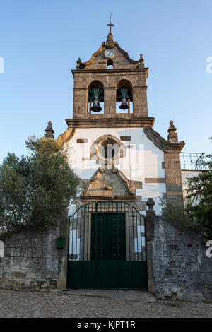 Parish church of Sao Romao with a truncated gable showing a rosacea window over the portal, double bells, clock and a cross, in Bacal, Braganca, Portu Stock Photo