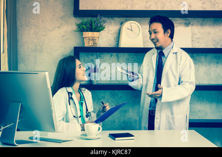 Couple of Asian doctors working with colleague which using technology computer in modern office of hospital, physician concept Stock Photo