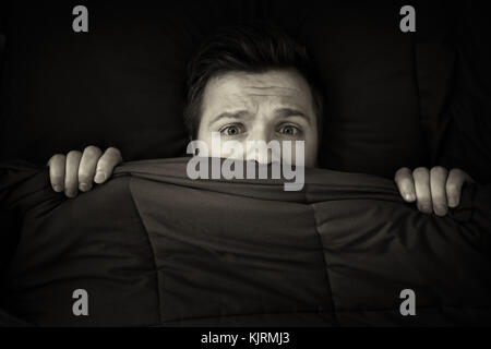 Caucasian young man hiding in bed under the blanket at home. Stock Photo