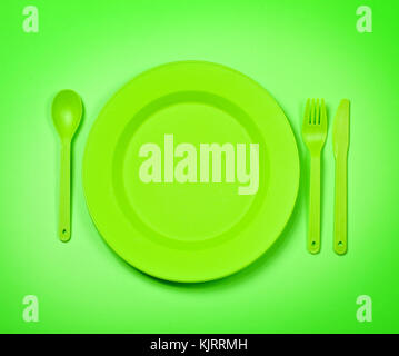 bright green  plastic disposable tableware, plates and forks, on bright green background Stock Photo
