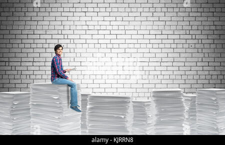 Attractive man sitting on pile of paper documents. Stock Photo