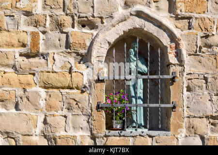 A small Madonna bronze statue with Jesus baby on its arm behind iron bars in a wall of a small church in Muggia, Italy Stock Photo