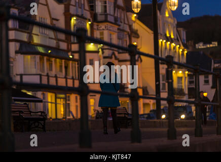 A woman alone walks along the Esplanade at Sidmouth as evening falls. Stock Photo