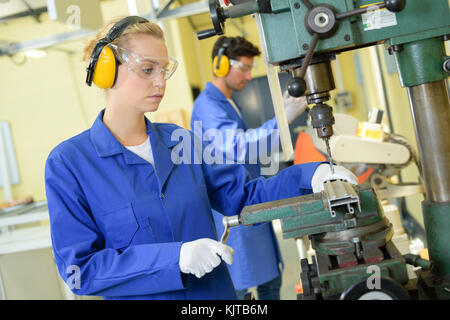 serious trainees focused on drilling metal piece with professional machinery Stock Photo