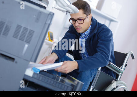wheelchair worker putting a stack of paper into printer Stock Photo