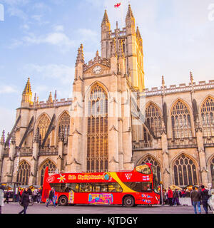 Sightseeing bus in front of Bath Abbey, a Gothic Church, Somerset, England.Christmas market stalls are on either side of the bus. Stock Photo