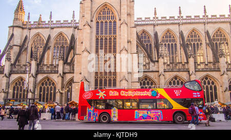 Sightseeing bus in front of Bath Abbey, a Gothic Church, Somerset, England.Christmas market stalls are on either side of the bus. Stock Photo