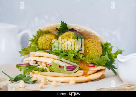 Fresh baked falafel in pita with vegetables, sprouts chickpeas and curry sauce. Vegan Healthy Food Concept. Stock Photo