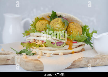 Fresh baked falafel in pita with vegetables, sprouts chickpeas and curry sauce. Vegan Healthy Food Concept. Stock Photo