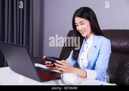 young business woman sitting at the desk with laptop and using mobile phone Stock Photo