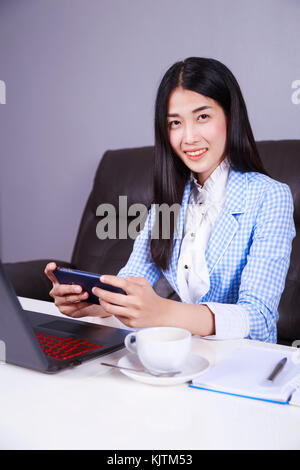 young business woman sitting at the desk with laptop and using mobile phone Stock Photo