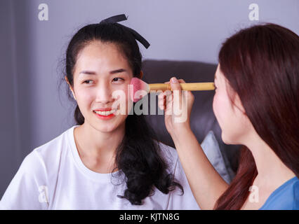 young woman using brush makeup on face her friend Stock Photo