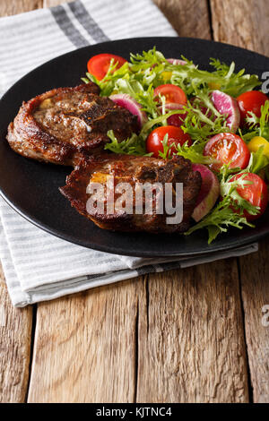 Delicious lamb steak and vegetable salad from radishes, tomatoes and lettuce close-up on a plate. vertical Stock Photo