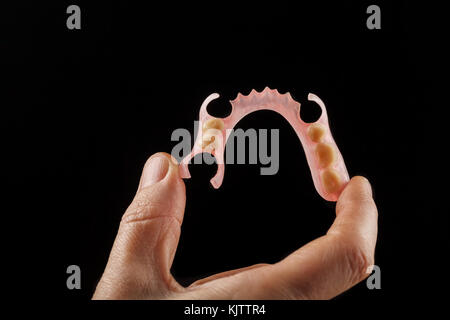 Dental prosthesis in the hand of the dentist. Close-up on a black background Stock Photo