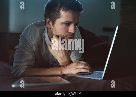 Caucasian young man lying on bed at his laptop. Working at home. Stock Photo