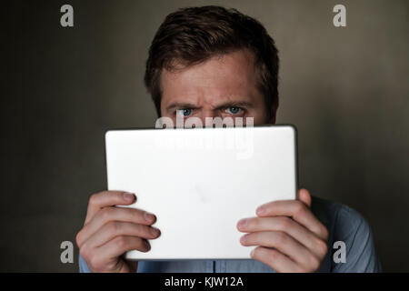 Serious mature middle aged man looking into tablet and frown his face. Stock Photo