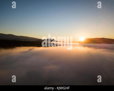 Beautiful aerial view of the ocean inlet covered in fog during a colorful sunrise. Taken in North Vancouver, British Columbia, Canada. Stock Photo