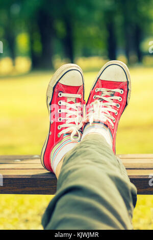 Woman's feet in a bright red canvas sneakers sitting on a bench Stock Photo