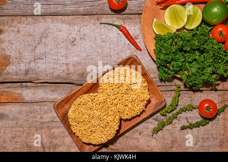 Raw asian instant noodles on wooden board with vegetables Stock Photo