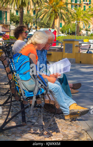 Hikers sat on bench reading Santa Margherita Italy Stock Photo