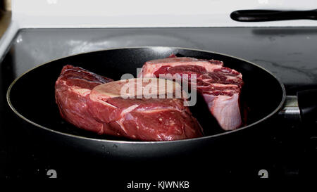 Side view of two raw pieces of meat shank in non-stick frying pan over a stove – cooking read meat concept Stock Photo