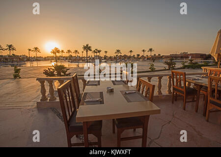 Outdoor dining terrace area with table set up on tropical ocean beach of luxury hotel resort at dusk sunset Stock Photo