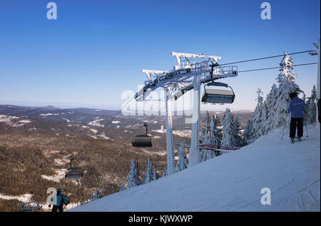 Mountain ski resort, the view from the top of the slopes of the valley. Skiers on a steep slope. The mast for the ski lift. Winter sport. Stock Photo