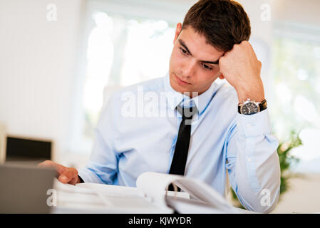 Young handsome pensive businessman working in the office. Stock Photo